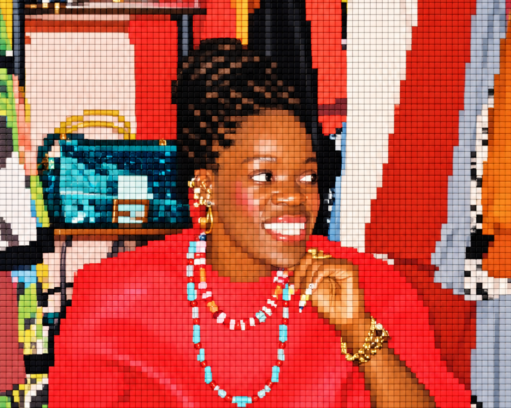 Smiling woman in a red dress and colourful jewellery sits in a zebra-print chair, posing confidently in a vibrant clothing shop.
