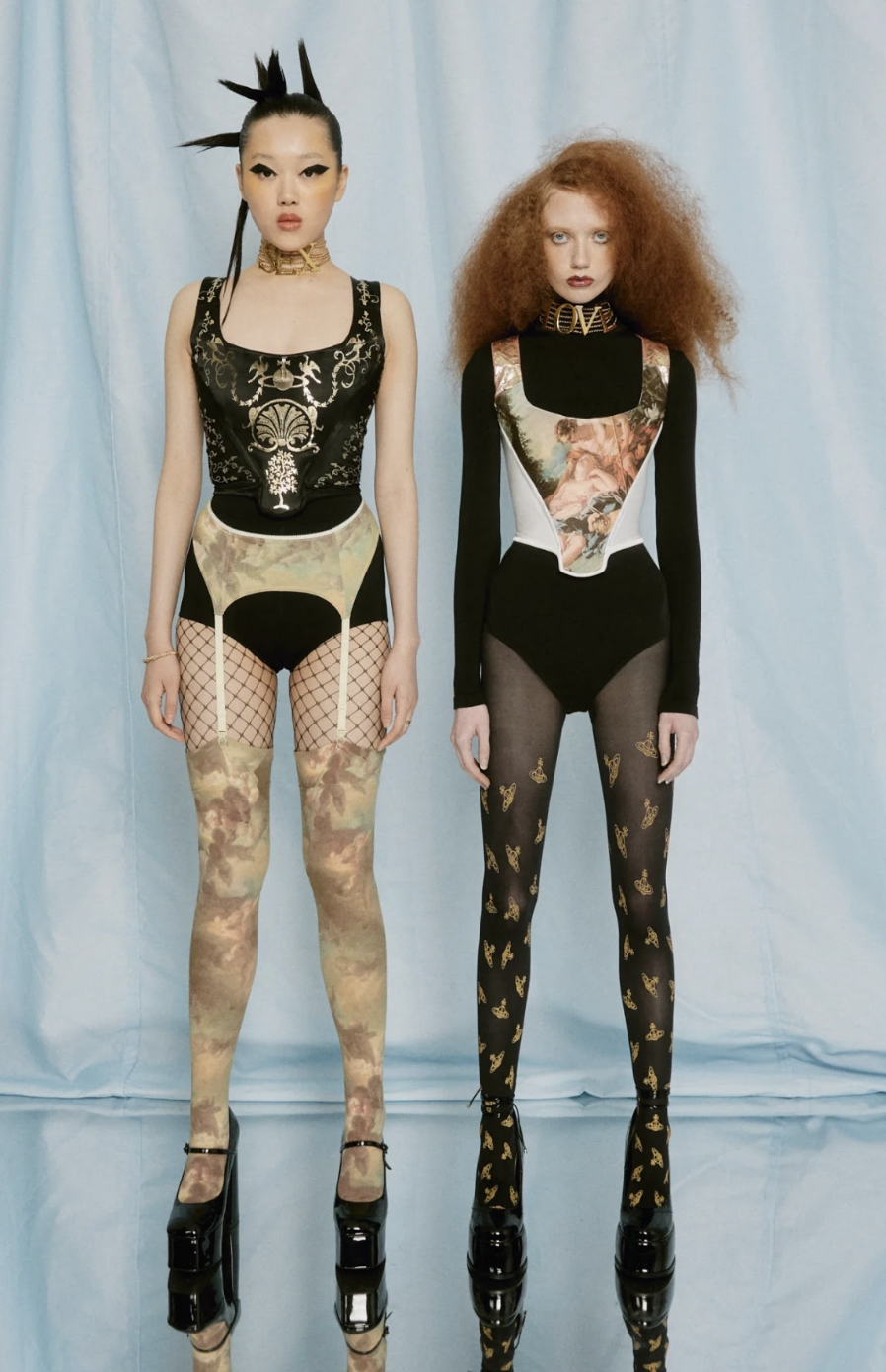 Two fashion models pose in avant-garde black bodysuits, patterned tights, platform heels, and dramatic hairstyles against a pale blue backdrop.