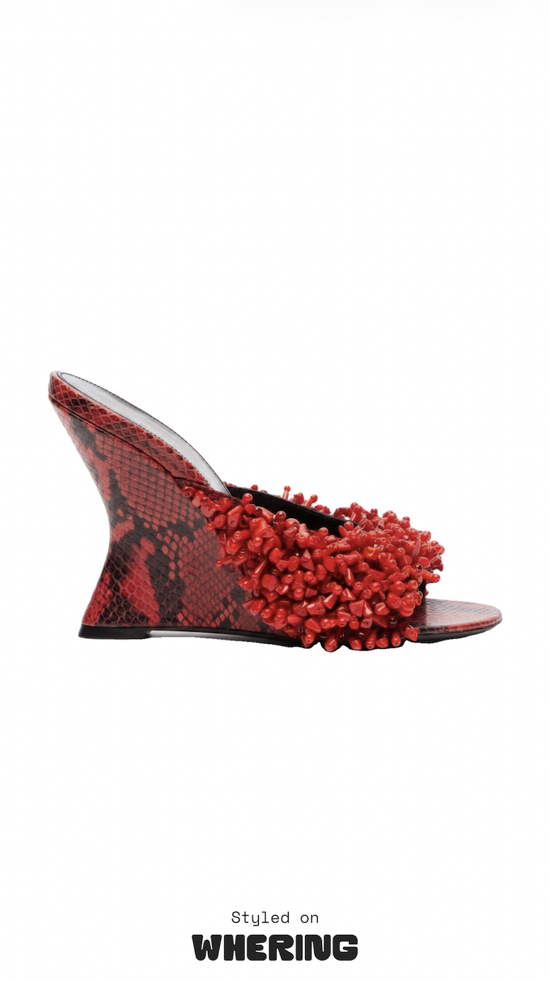 Red-and-black sculptural high-heeled shoe with a snakeskin pattern and dense red crystal embellishments, isolated on white; styled on WHERING.