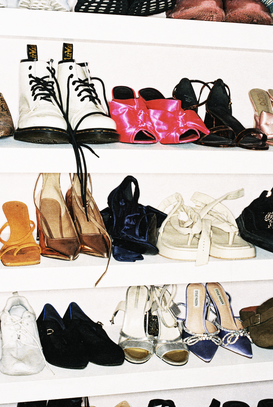 Shelves display an eclectic shoe collection: white combat boots, hot-pink heels, sandals, sneakers, flats, and black footwear in a wardrobe.